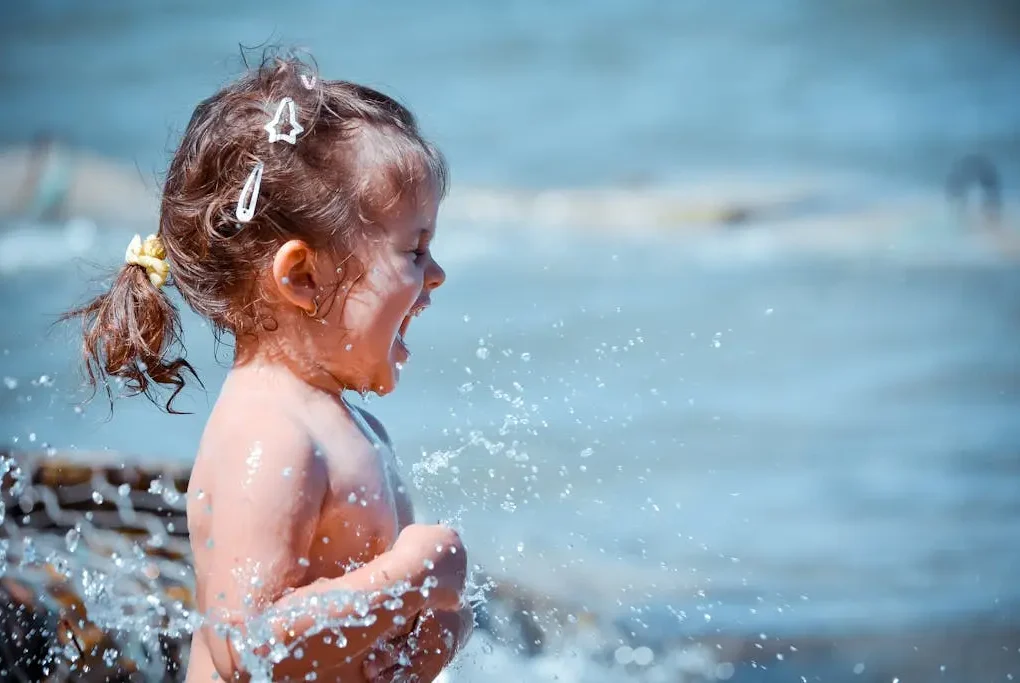 O que fazer na Praia Grande com crianças. Menina pequena brincando na água do mar.